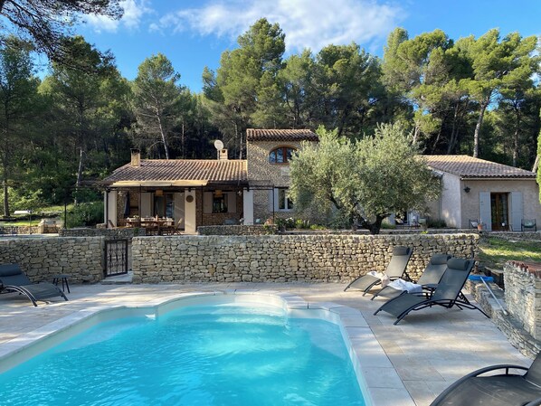 A stone-walled swimming pool with lounge chairs, a stone house with a tiled roof, and surrounding trees. - Large Mas in the Roussillon pine forest, heated swimming pool (Gargas)