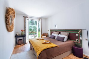 A bedroom with a large bed, a bedside table, a chair, and a view of the outdoors. - Large Mas in the Roussillon pine forest, heated swimming pool (Gargas)