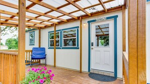 Eine überdachte Veranda mit Holzterrasse, einem blauen Stuhl und einem Willkommensschild.