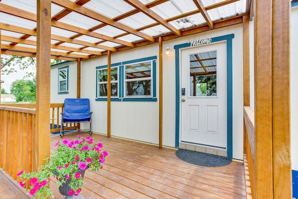 A covered porch with a wooden deck, a blue chair, and a door marked "Welcome". - Northeast Texas Vacation Rental ~ 6 Mi to Commerce (Commerce)