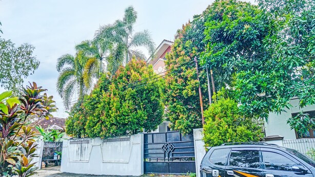 Área residencial com portão fechado, um carro preto estacionado em frente e vegetação exuberante.
