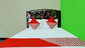Uma cama com colcha estampada em vermelho e branco, duas almofadas vermelhas e cabeceira acolchoada.