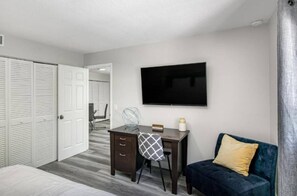 A hotel room with a bed, a desk with a chair, a TV, and a blue sofa. - 🌴 Beach Getaway | Hot Tub | Pets OK! | Fire Pit 🌴 (West Palm Beach)