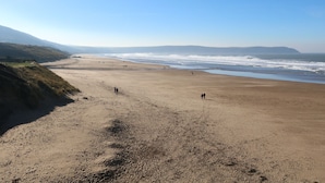 Ein weiter Strand mit sanften Wellen, wolkenlosem Himmel und Hügeln in der Ferne.