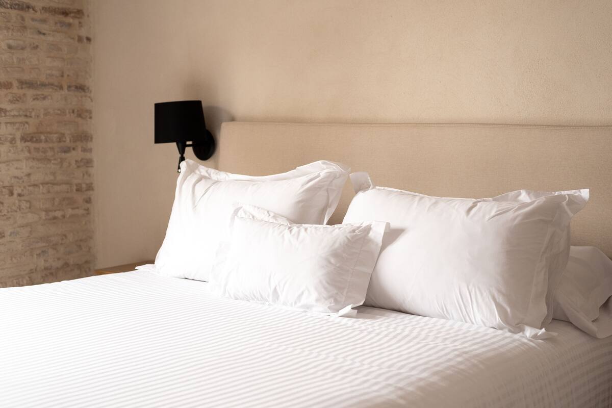 A neatly made bed with white linens and a black wall-mounted lamp.