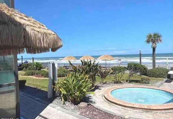 A pool area with a thatched roof structure, a circular pool, and a view of the beach and ocean.