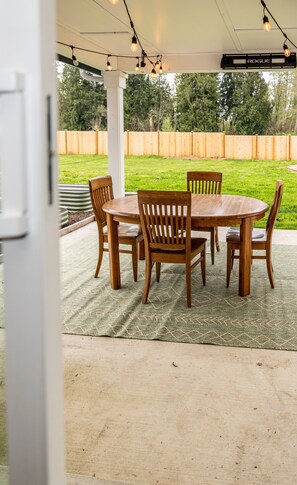 An outdoor patio with a wooden table and chairs, surrounded by a green lawn and a wooden fence. - Home in Lake Stevens with large fenced yard (Lake Stevens)