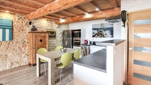 Una cocina rústica con paredes de piedra, vigas de madera y un comedor con mesa y sillas.