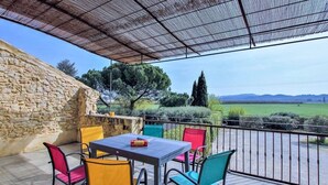 Un patio al aire libre con un muro de piedra, una mesa con sillas y vistas al campo.