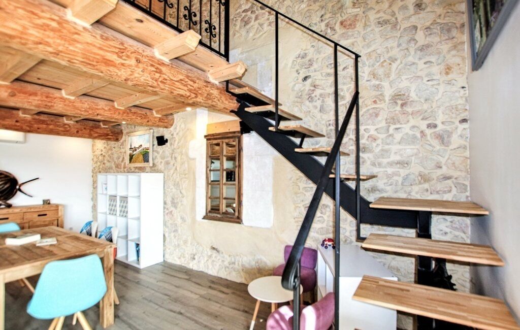 A rustic interior with exposed wooden beams, a stone wall, and a black staircase.