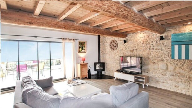 Una sala de estar moderna con una pared de piedra, techo de madera, un sofá, un televisor y una chimenea.