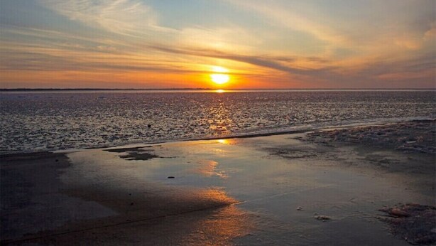 A sunset over a beach with a calm sea and a clear sky.