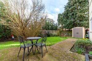 Ein Garten mit einem Metalltisch und -stühlen, einem Holler Shed und einem großen Baum.