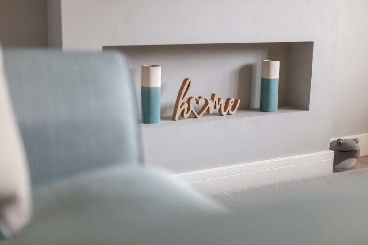 Un salón con un sofá azul claro, una chimenea con un estante que muestra un letrero que dice 'hogar' y dos velas.