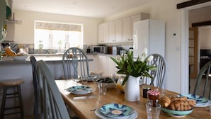 Una cocina con una mesa lista para el desayuno, con cruasanes y un jarrón de flores.