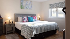 Un dormitorio con cama, dos mesitas de noche, una ventana con cortinas y una obra de arte colgada en la pared.
