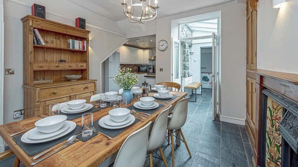 Een eetgedeelte met een houten tafel voor vier personen, een kroonluchter en een boekenkast met boeken en speakers.