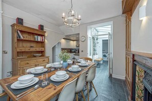 Un coin repas avec une table en bois dressée pour quatre personnes, un lustre et une bibliothèque contenant des livres et des haut-parleurs.