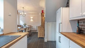 Een moderne keuken met donkere betegelde vloer, houten aanrechtbladen en witte kastjes.