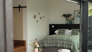 A modern bedroom with a bed, bedside table, and a small stool. - Subterranean Studio with Panoramic Views & Sauna (Pembrokeshire)
