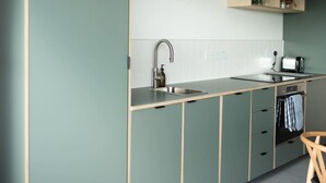 A modern kitchen with a single sink, a built-in oven, and a wooden chair. - Subterranean Studio with Panoramic Views & Sauna (Pembrokeshire)