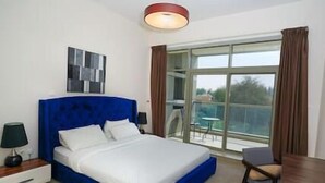 Habitación de hotel con una cama grande, una mesita de noche, un escritorio y una silla. Se ve un ventanal con cortinas y vistas al exterior.