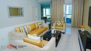 A modern living room with a sofa, armchair, and a coffee table. There is a large window with curtains, a flat-screen TV, and a small side table with a vase. - Cozy 2BR apartment in Downtown Dubai (Dubai)