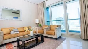 A modern living room with a sofa, armchair, and coffee table. There is a large window with curtains and a view of buildings.