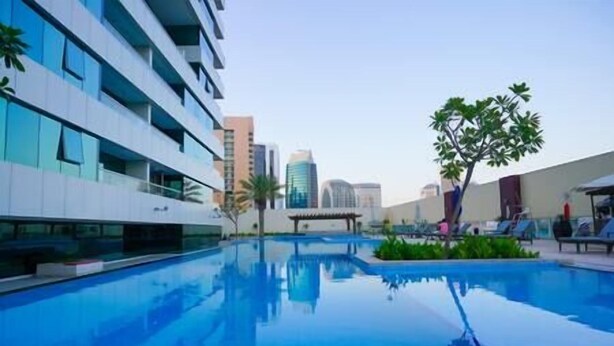 A modern hotel with a swimming pool, reflecting nearby buildings.