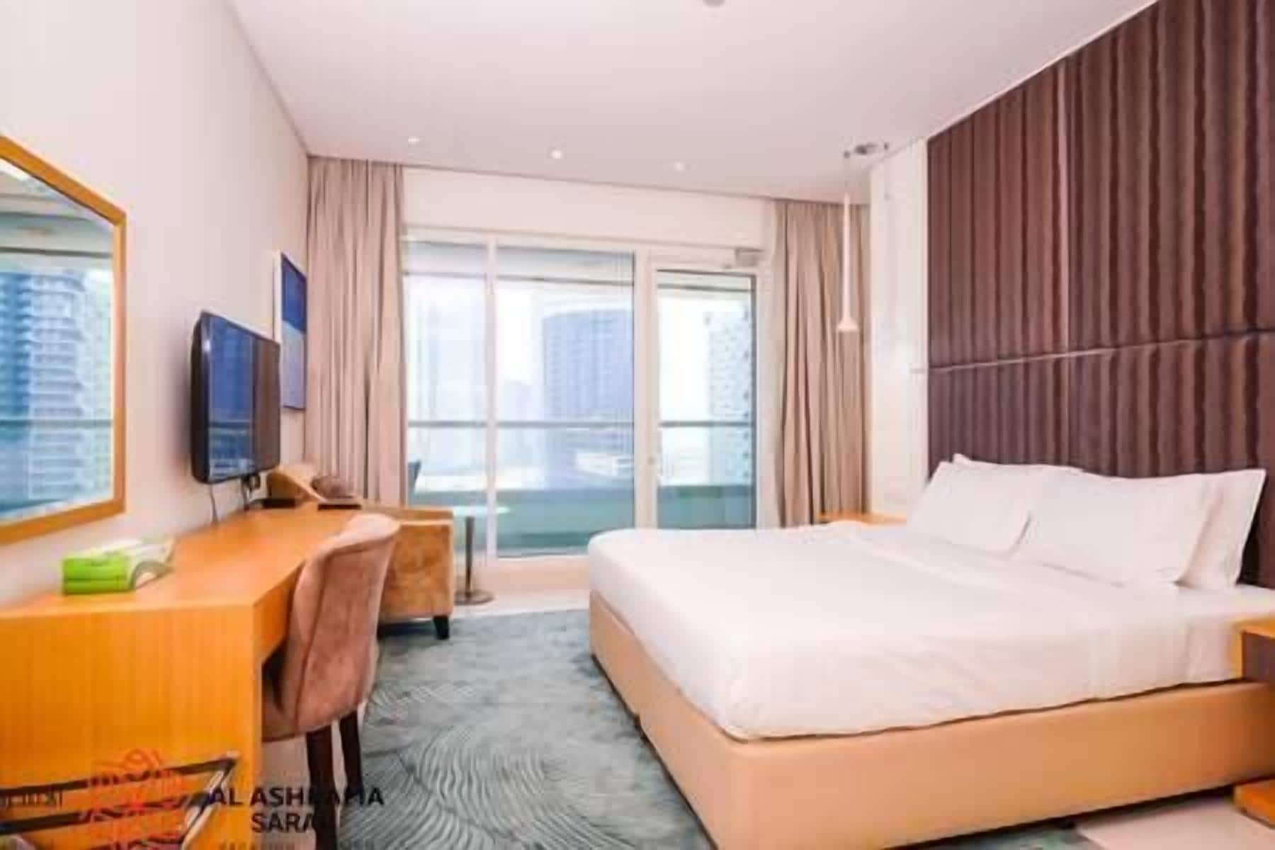 A hotel room with a large bed, a desk with a chair, a television, and a window with curtains.
