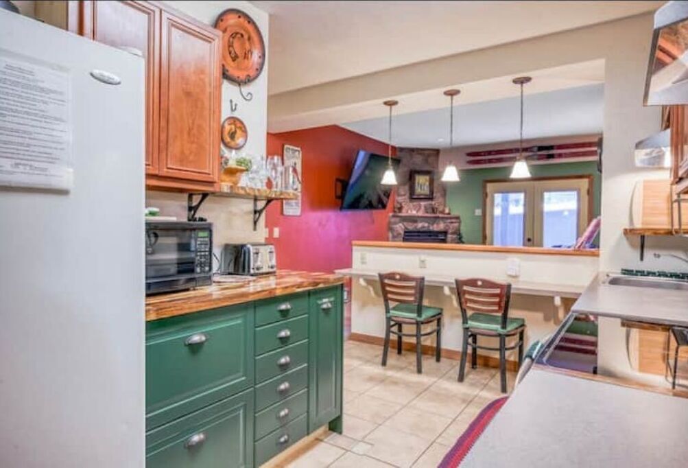 A kitchen with green cabinets, a microwave, and a wooden countertop. There are two chairs and a small table.