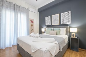 A bedroom with a bed, two bedside tables with lamps, a wall-mounted air conditioner, and a window with curtains. - Elegant Suite by Cloudkeys (Athens)