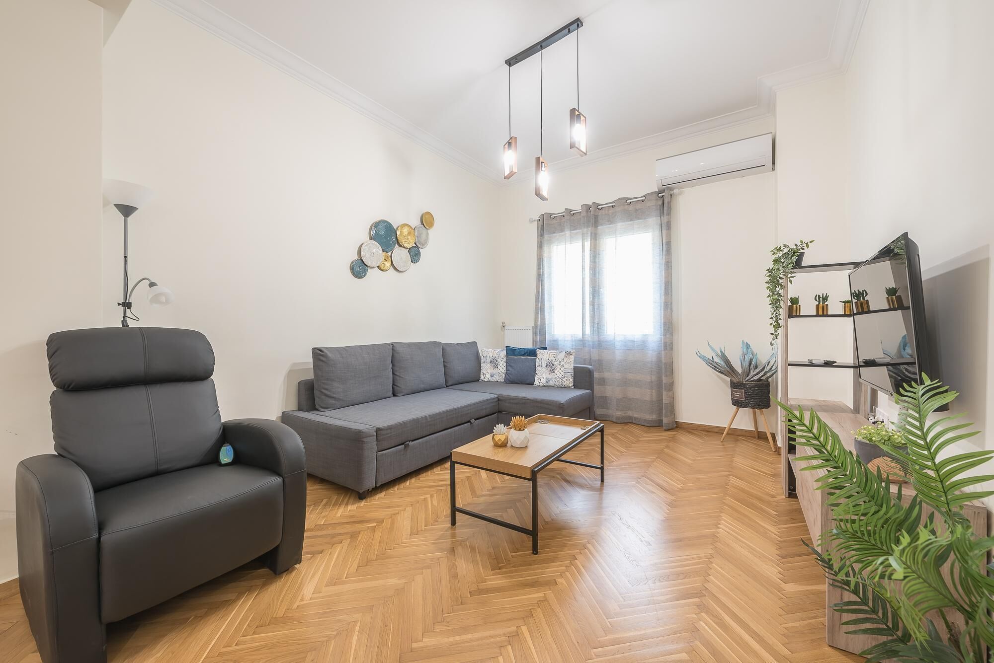 A modern living room with a grey sofa, a black armchair, a wooden coffee table, and a TV on a black stand.