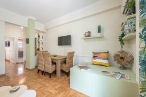 Ein Essbereich mit Holztisch und Korbstühlen, einem an der Wand befestigten Fernseher und einem kleinen Regal mit Dekoration.