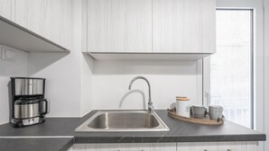 Una cocina moderna con un lavamanos de acero inoxidable, una cafetera y una bandeja con tazas y un hervidor.