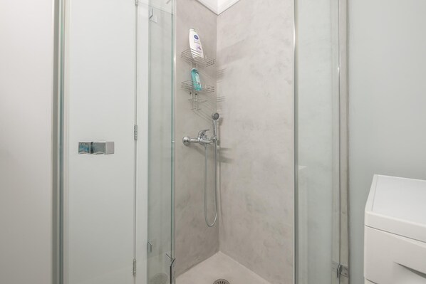 Cabina de ducha con paredes de vidrio, cabezal de ducha de mano y grifo empotrado.