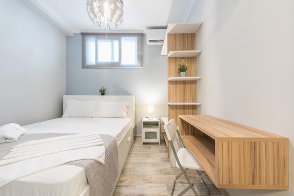 A modern bedroom with a bed, bedside table, lamp, and built-in wooden shelving unit.