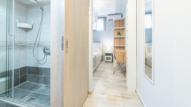 Een moderne badkamer met een douchecabine van glas, een houten wastafelmeubel en een klein nachtkastje met een lamp.