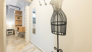 Een gang met een houten vloer, een witte muur met een afbeelding van een vogelkooi, en een houten kast met planken.