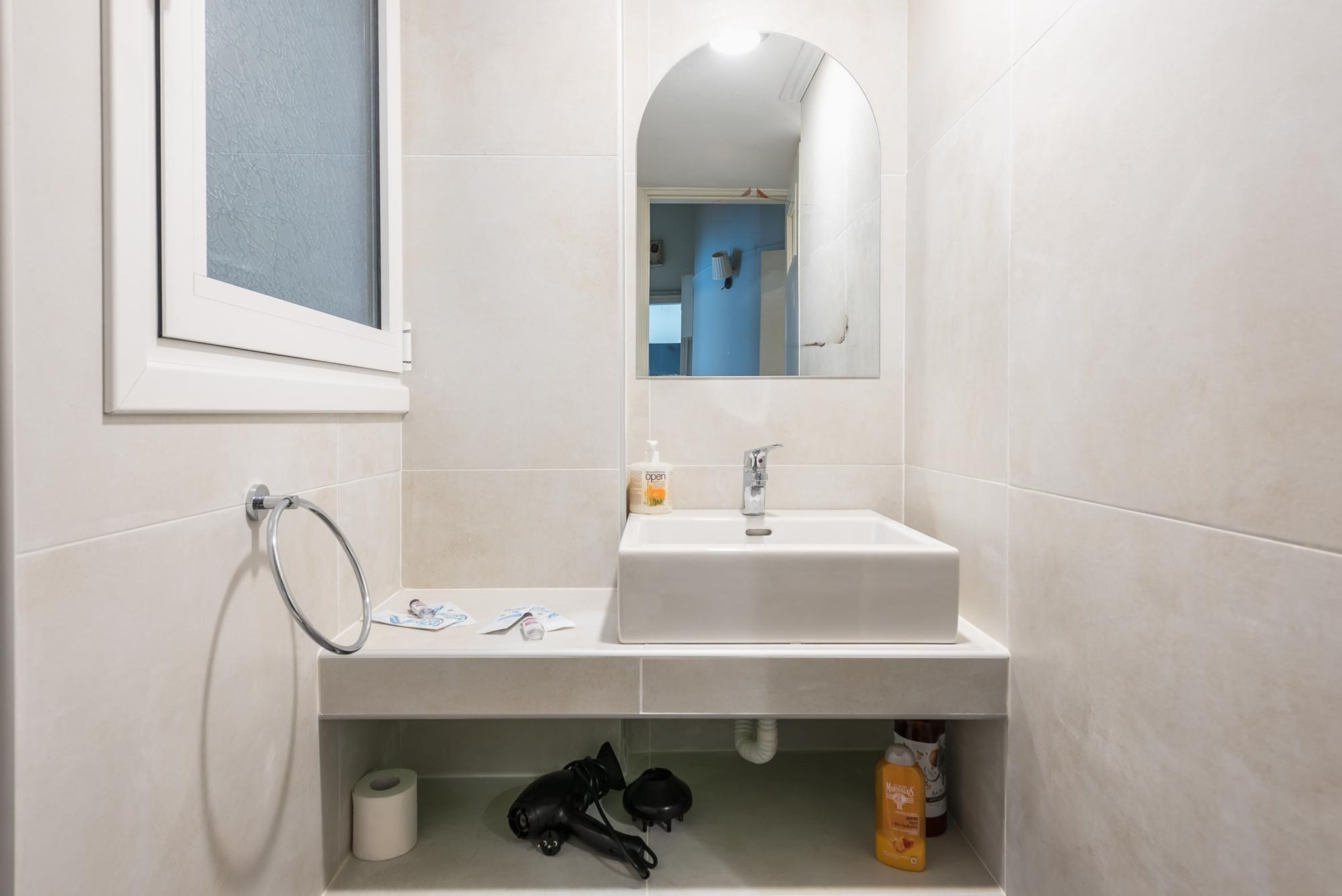 Une salle de bain avec un lavabo blanc, un miroir, un porte-serviettes et un rouleau de papier toilette.