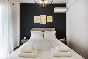 A hotel room with a large bed, two bedside tables, a wall-mounted air conditioner, and three framed artworks above the bed. - Atmospheric Apartment Near Acropolis by Cloudkeys (Athens)