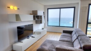 A modern living room with a flat-screen TV, built-in shelves, a grey sofa, and a large window overlooking the ocean. - Bright & cozy 3bedrooms with stunning views DLAP1-1 (Sliema)