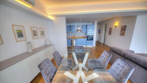A modern living room with a glass dining table, grey upholstered chairs, a grey sofa, and a kitchen in the background. - Bright & cozy 3bedrooms with stunning views DLAP1-1 (Sliema)