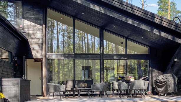 A modern building with large glass windows, a wooden deck, and outdoor seating.