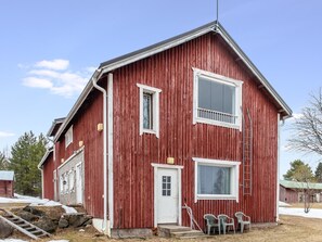 A red wooden house with a white door and windows, a garage, and a small porch with chairs.