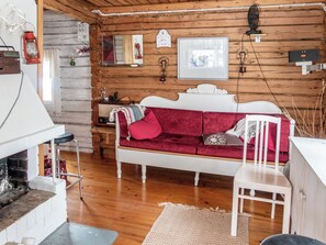 L’intérieur d’un chalet accueillant, avec un mur en bois, un canapé blanc agrémenté de coussins rouges, une chaise blanche, une petite table avec une radio et une cheminée.