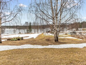 A snowy landscape with a tree in the foreground, a body of water in the background, and a clear sky.