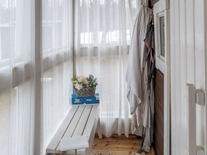 Ein Zimmer mit einer Holzbank, einem Blumenkorb und einem Fenster mit durchsichtigen Vorhängen.