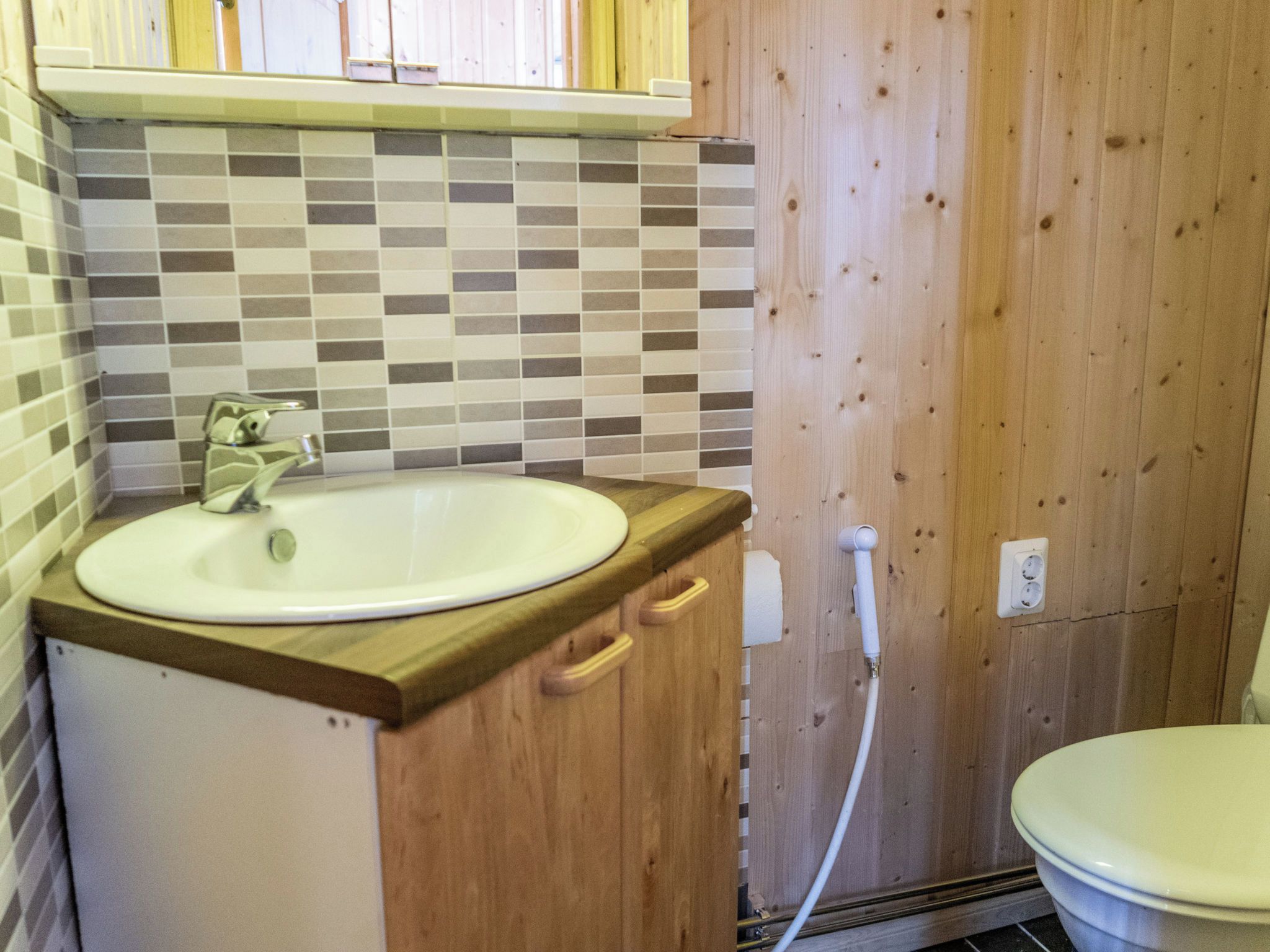 A bathroom with a white sink, wooden cabinet, and a tiled backsplash.