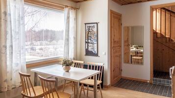 Un área de comedor con una mesa y sillas, una ventana con cortinas, un cuadro en la pared y una escalera que conduce a otra habitación.